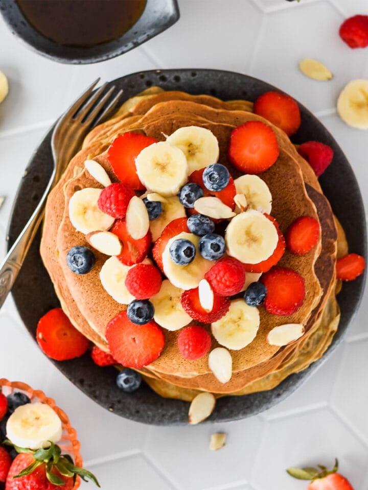 Stack of paleo pancakes topped with lots of banana, blueberries, strawberries and raspberries.