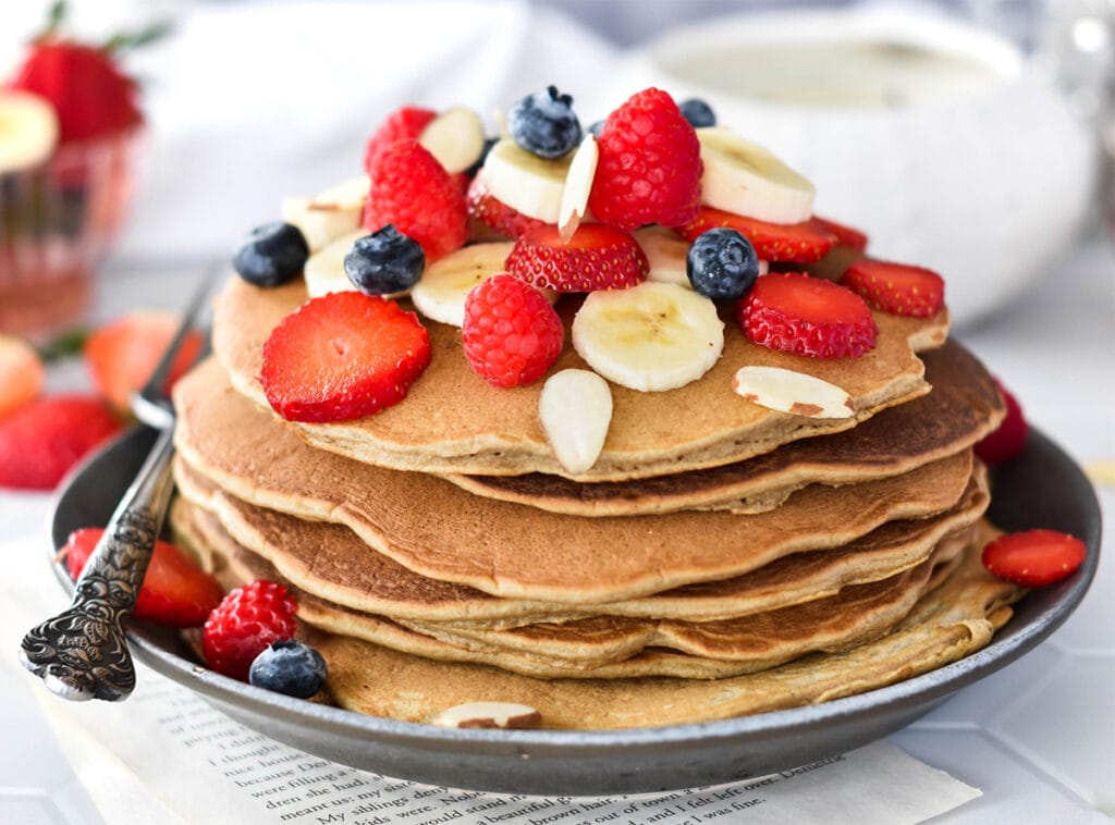 Stack of paleo banana flour pancakes topped with lots of banana, blueberries, strawberries and raspberries.