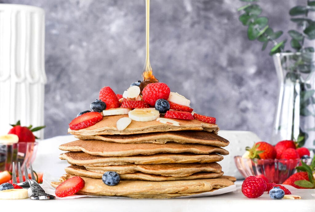 Stack of paleo pancakes topped with lots of banana, blueberries, strawberries and raspberries.