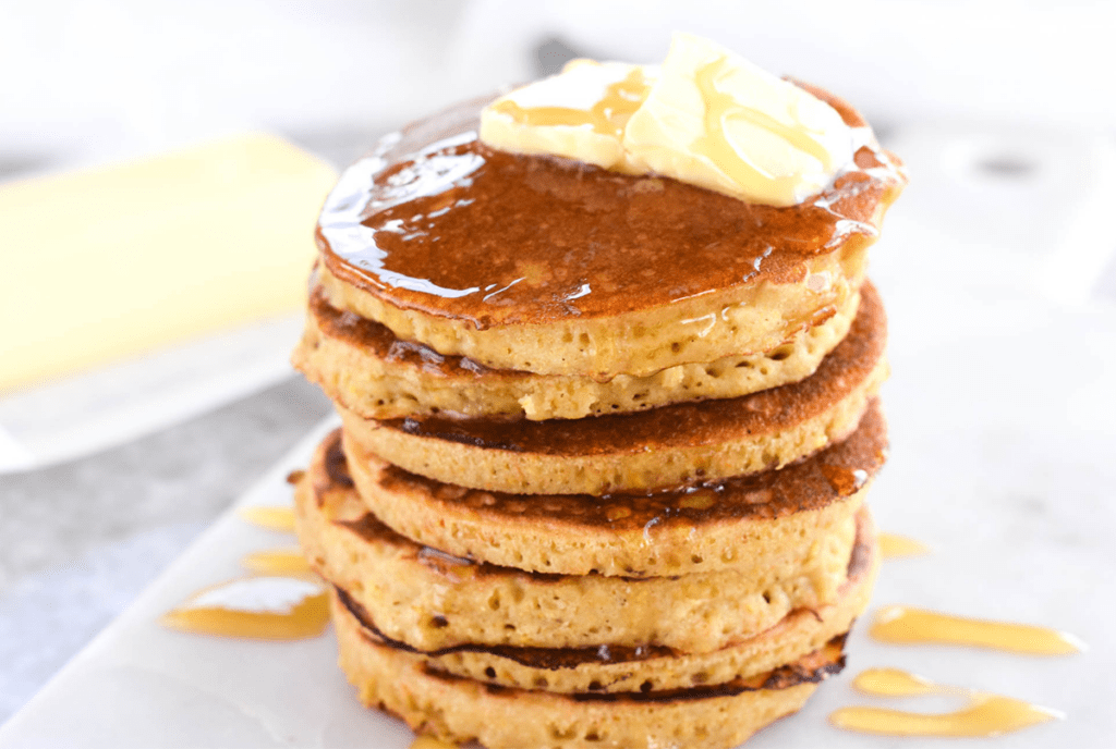 High stack of pancakes with melted butter and honey on top.