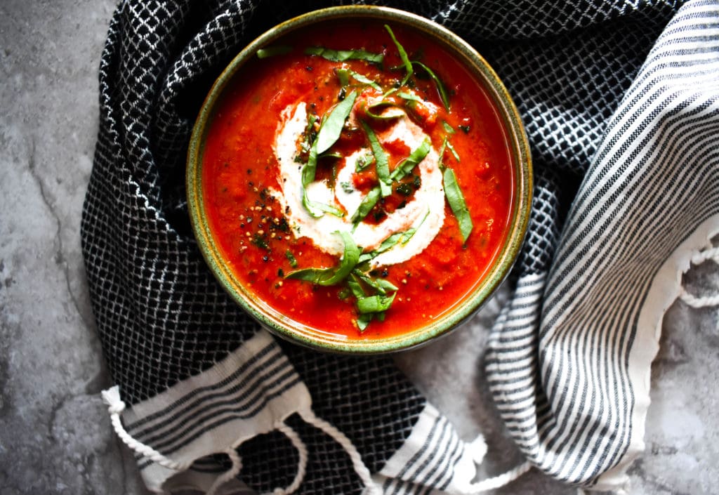 Bright red tomato soup with coconut cream swirled in it.