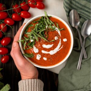 Hand holding owl of healthy paleo tomato soup topped with basil and coconut cream.