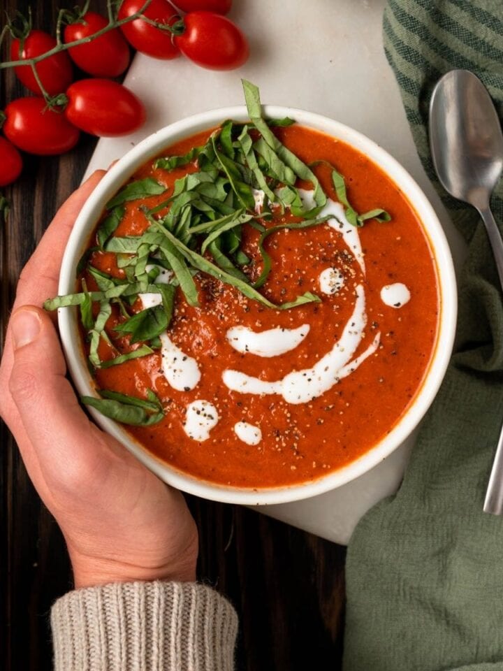 Hand holding owl of healthy paleo tomato soup topped with basil and coconut cream.