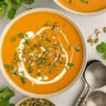 Two bowls of curry apple butternut squash soup topped with pumpkin seeds, sunflower seeds, coconut milk, and cilantro.