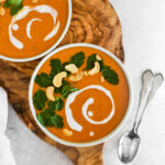 Two bowls of bright orange paleo curry butternut squash soup with cilantro, coconut cream and cashews on top.