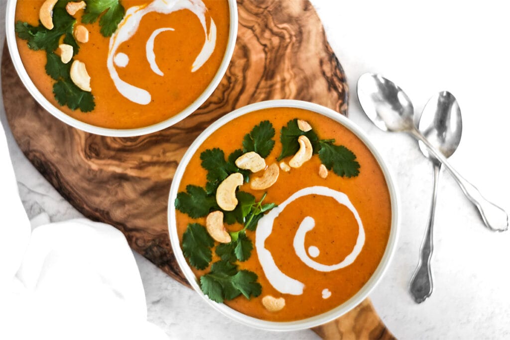 Two bowls of bright orange paleo curry butternut squash soup with cilantro, coconut cream and cashews on top.