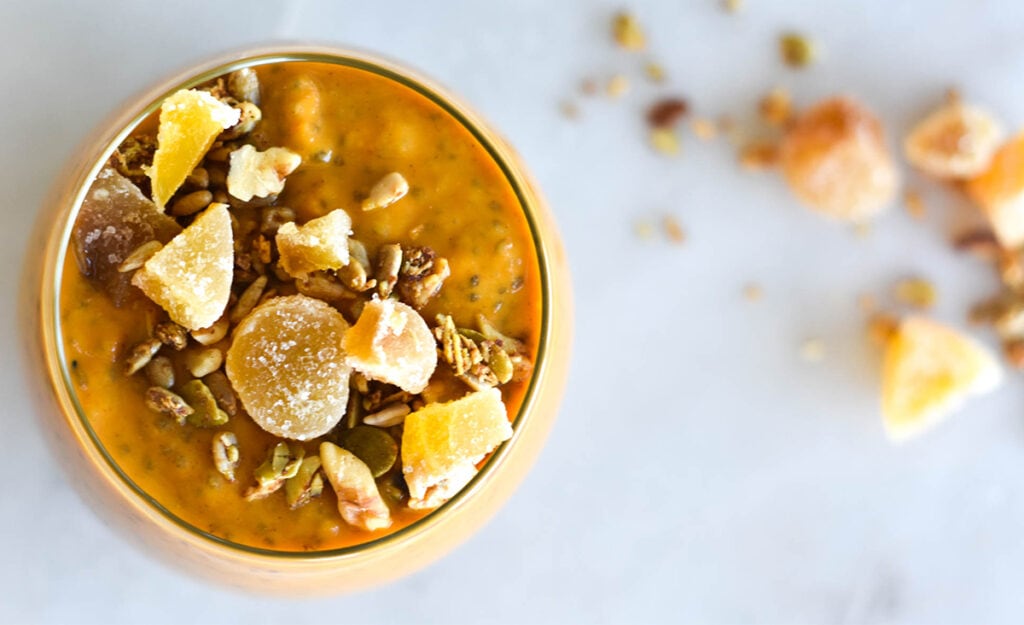 Top down view of bright orange pumpkin chia pudding on cutting board next to spice and nuts.