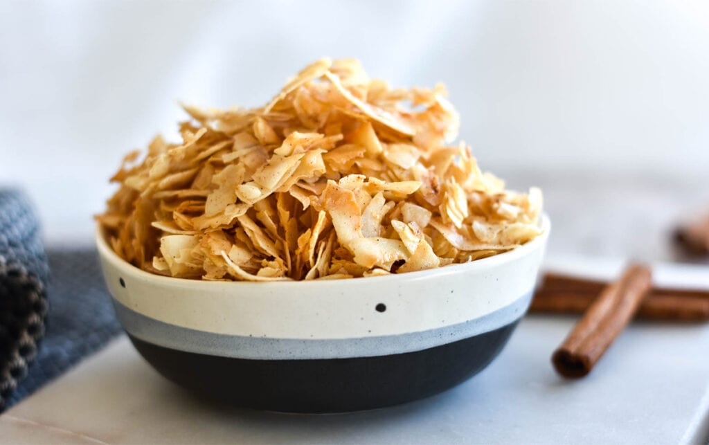 Bowl of coconut chips next to cinnamon sticks