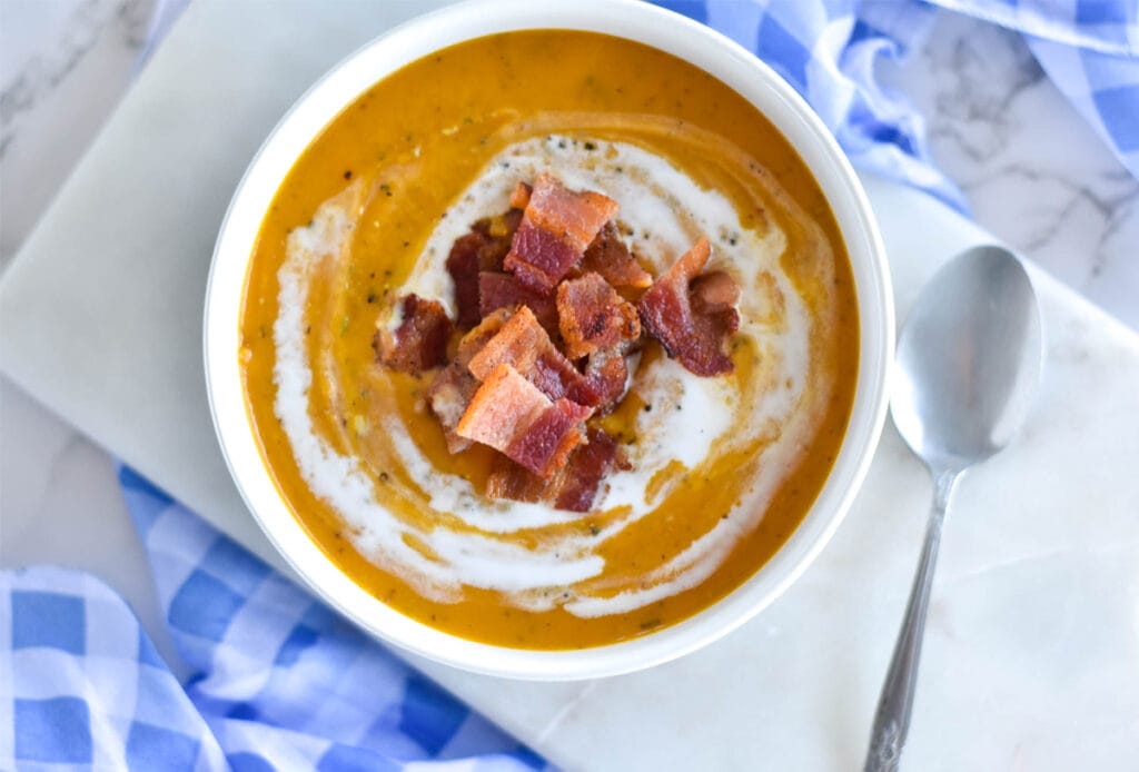 white bowl filled with sweet potato soup topped with bacon on checkered napkin.