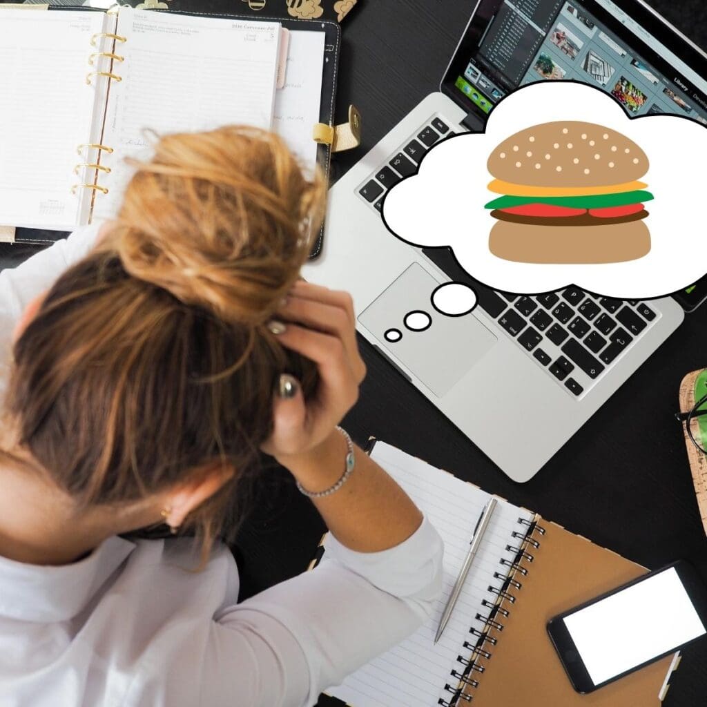 Girl looking stressed out over her computer. She has a thought bubble with a cheeseburger in it.