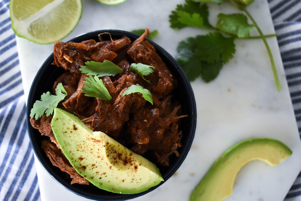 Top down view of barbacoa in bowl with avocado and cilantro.