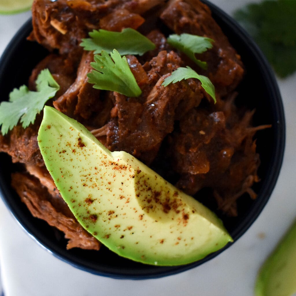 Top down view of barbacoa in bowl with avocado and cilantro.