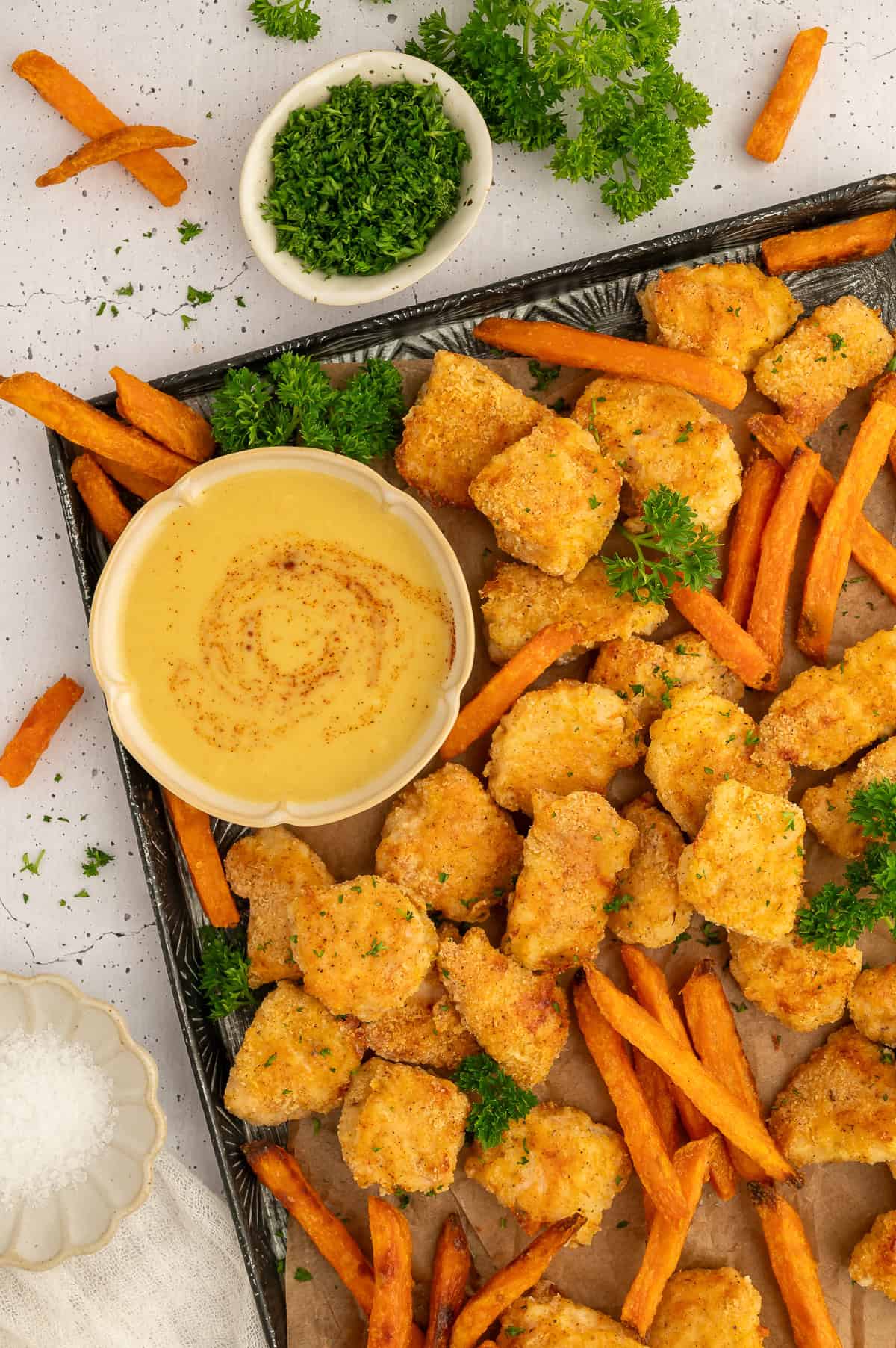 Pan with golden paleo chicken nuggets, sweet potato fries, parsley, and honey mustard on it.