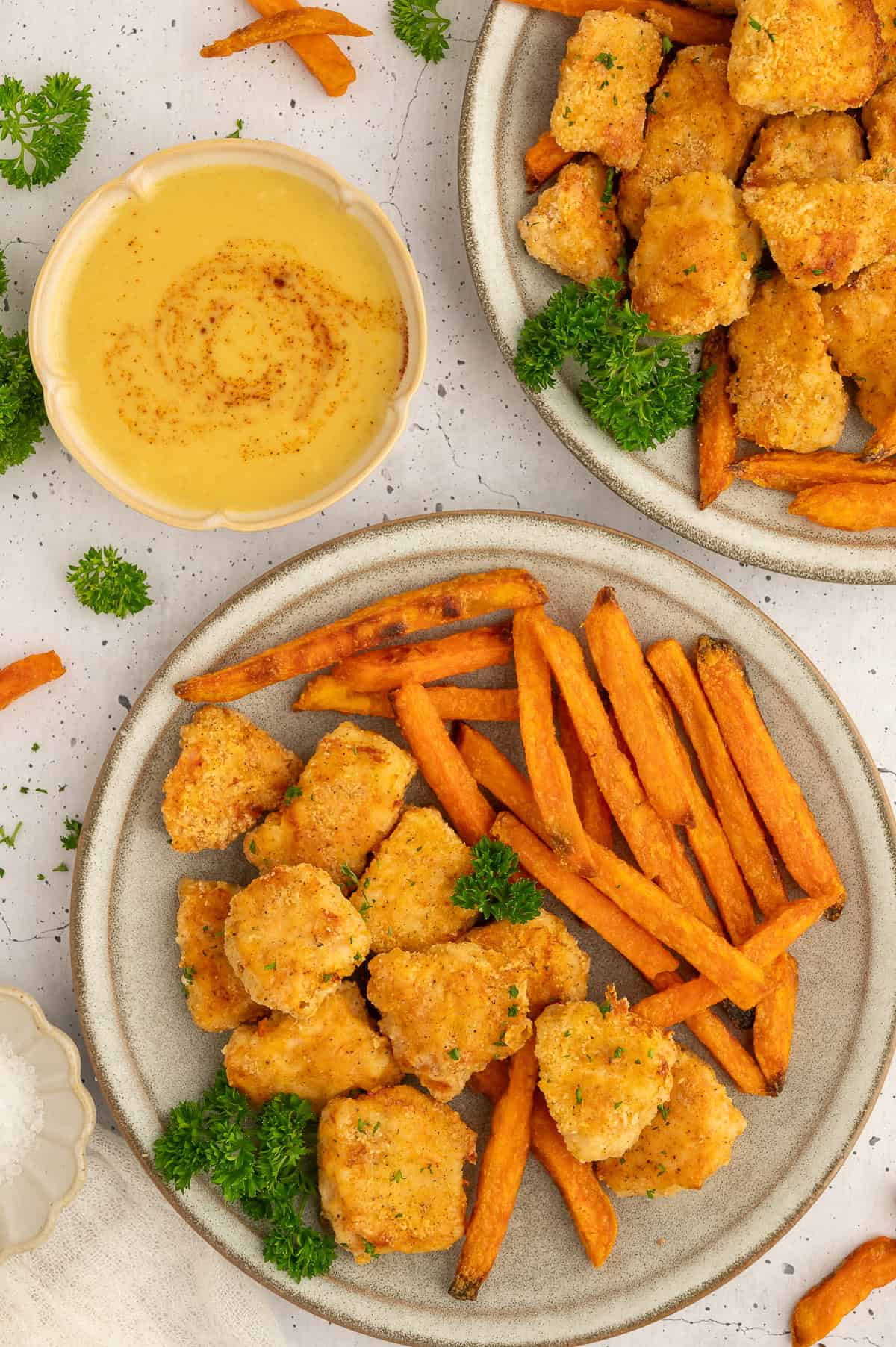 Plate with golden paleo chicken nuggets, sweet potato fries, and parsley on it.