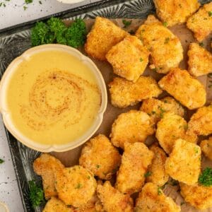 Pan with golden paleo chicken nuggets, parsley, and honey mustard on it.