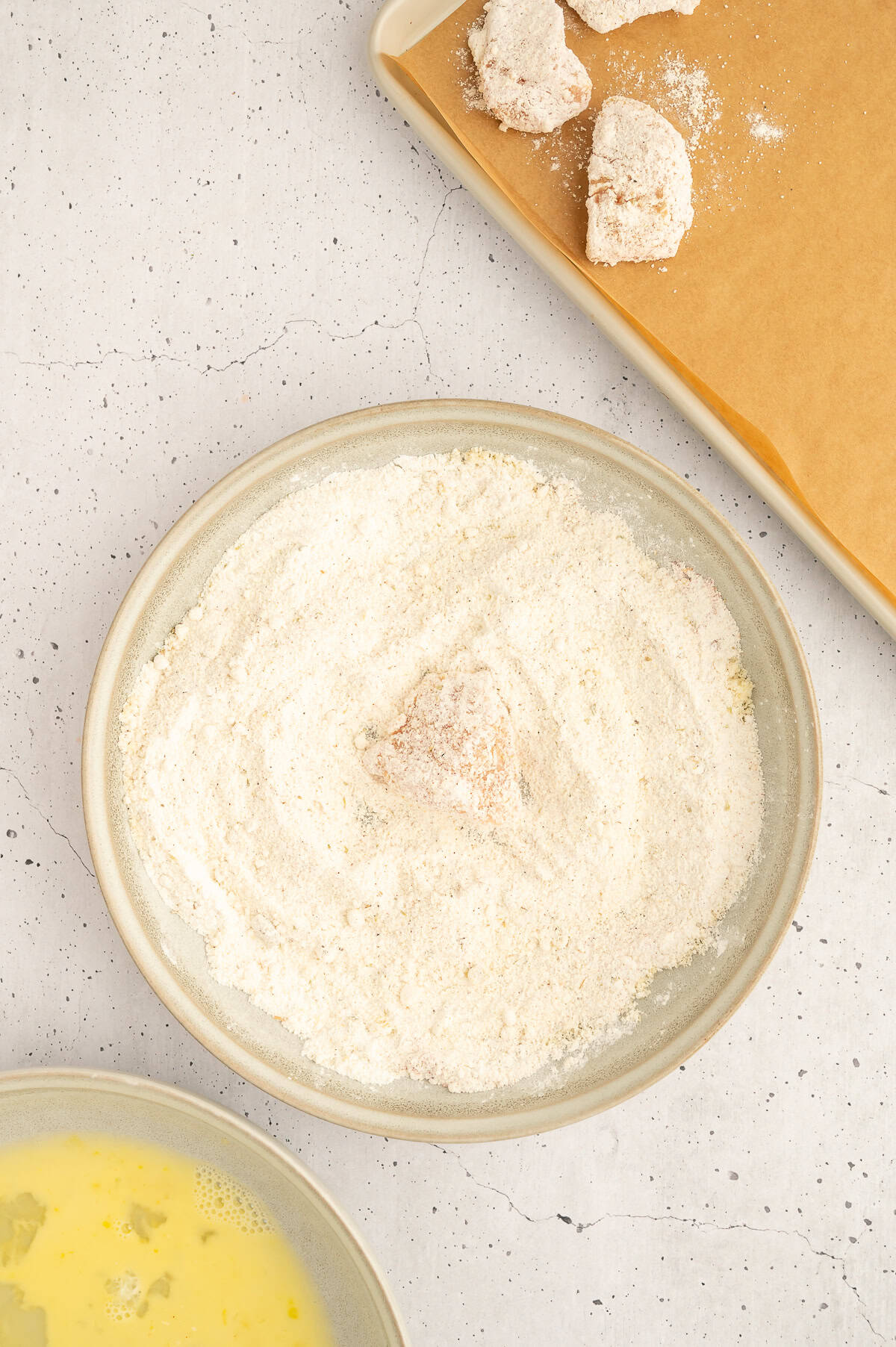 Chicken breast getting dipped into breading mixture.
