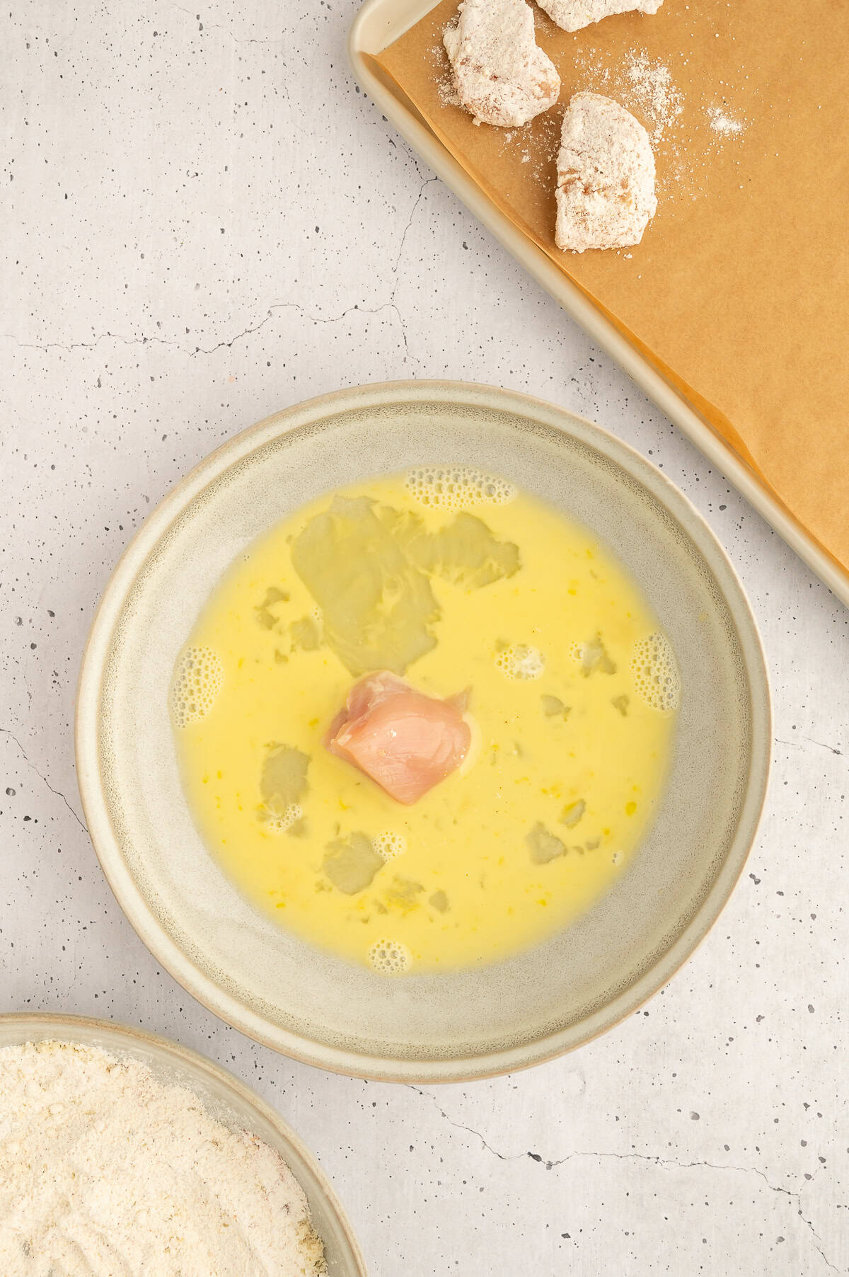 Chicken breast getting dipped into egg.