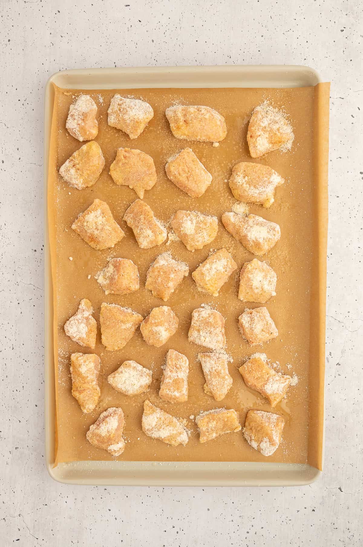 Uncooked paleo chicken nuggets on a parchment paper lined sheet pan.