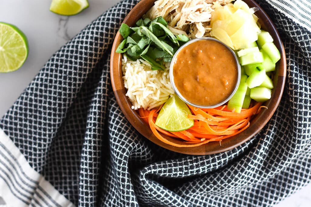 Wooden bowl filled with ginger, basil, rice, cucumber and chicken wrapped in a towel.