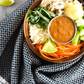 Wooden bowl filled with ginger, basil, rice, cucumber and chicken wrapped in a towel.