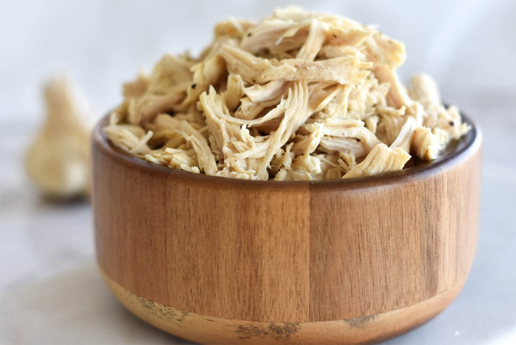 Bowl of shredded chicken next to garlic