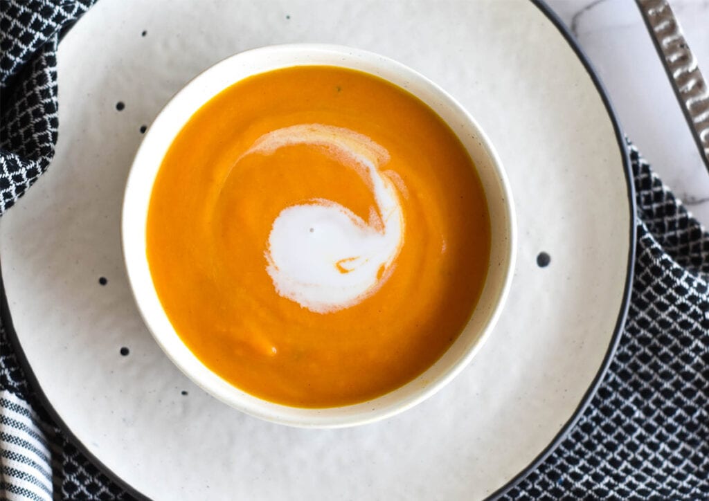 Top down view of carrot ginger soup with a white swirl of coconut cream.