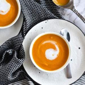 Bowl of brightly colored carrot ginger soup on a plate.