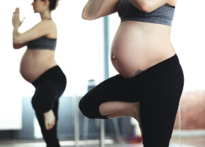 Pregnant woman in sports bra and leggings doing yoga.