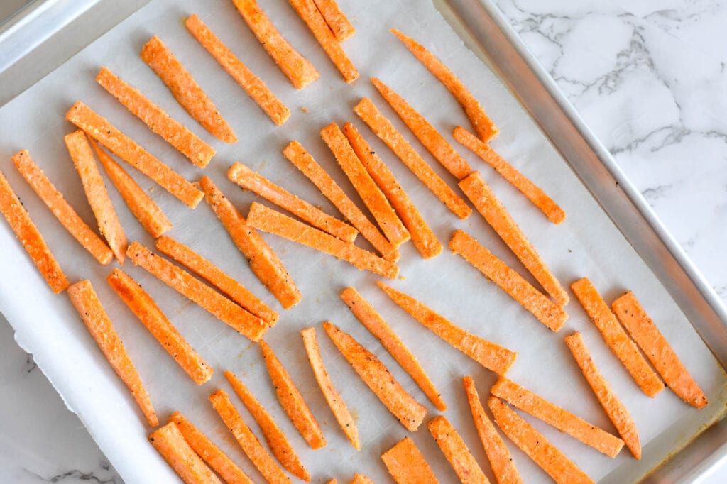 sweet potato fries laying on sheet pan with parchment paper.