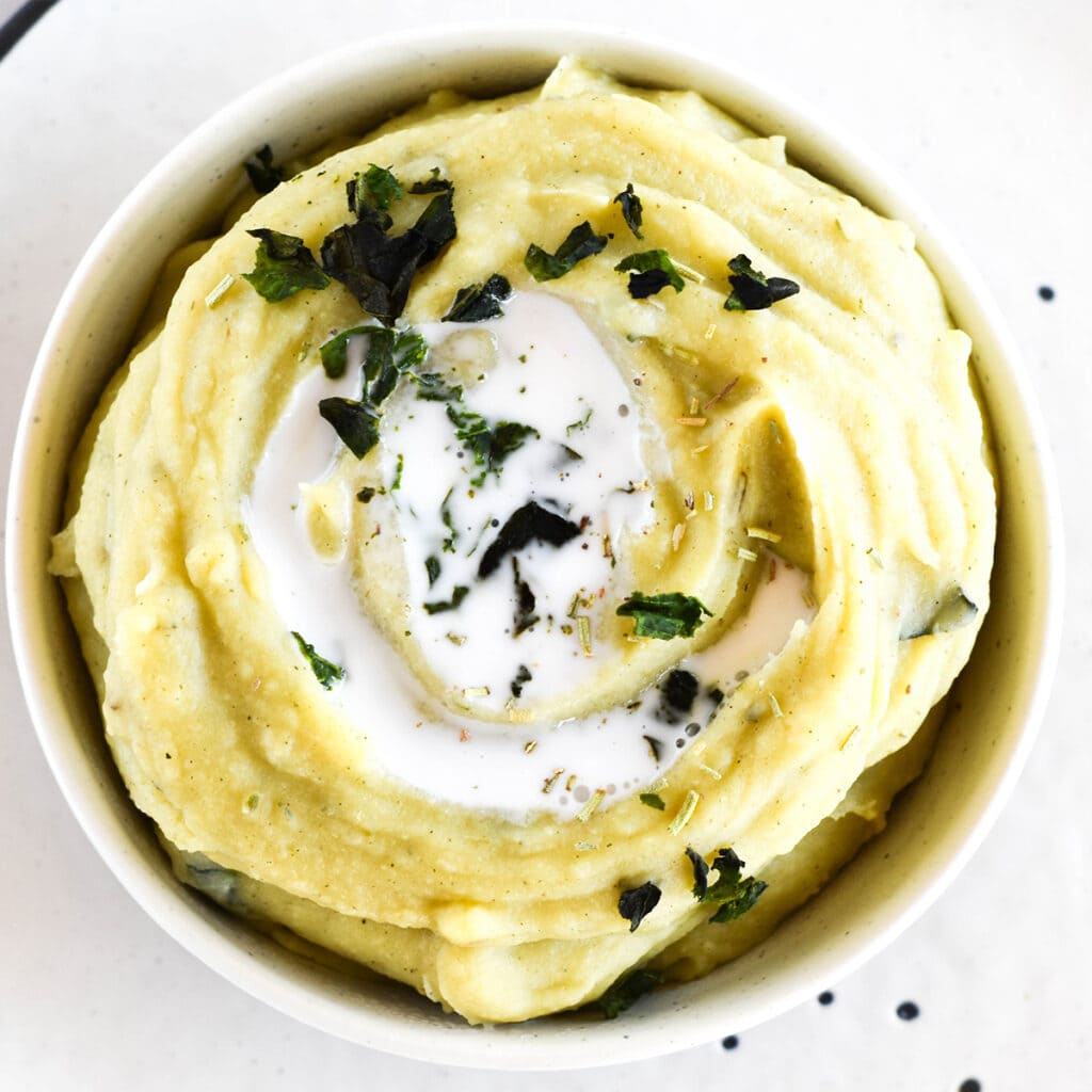 Top down view with white bowl of creamy mashed white sweet potatoes with herbs and coconut milk.