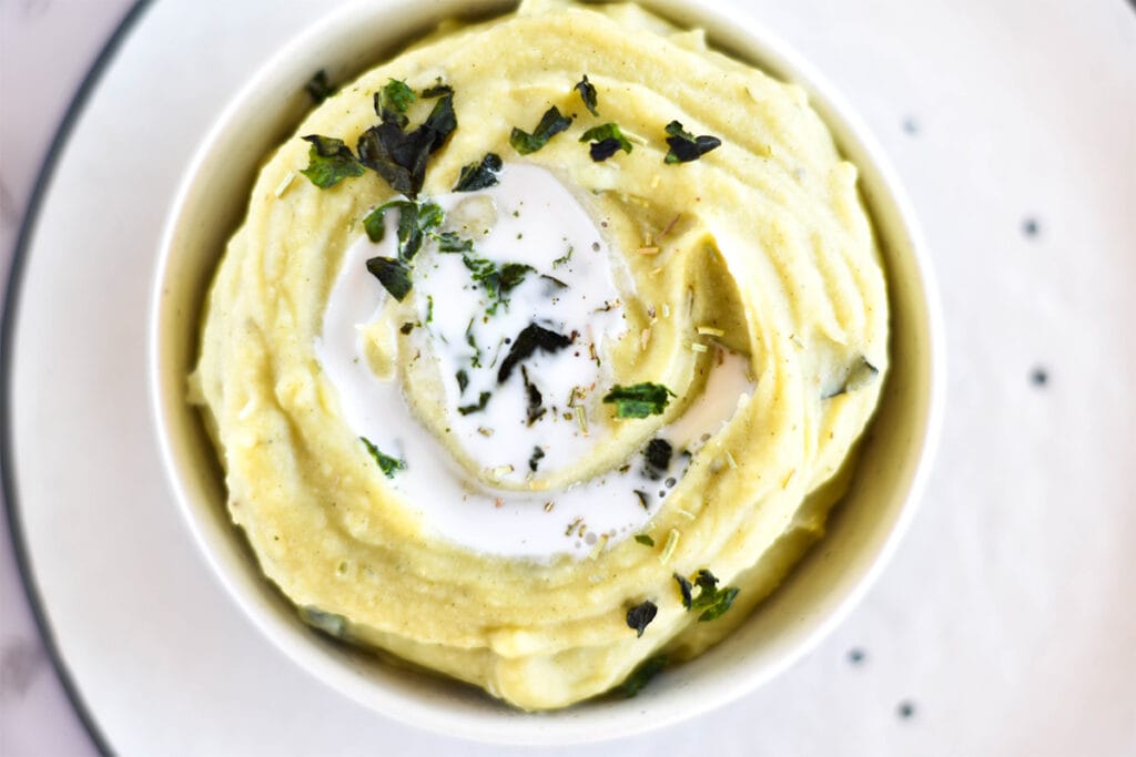 Top down view with white bowl of creamy mashed white sweet potatoes with herbs and coconut milk.