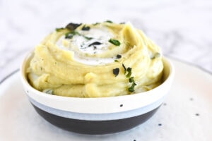 Bowl of mashed potatoes topped with coconut milk and herbs.