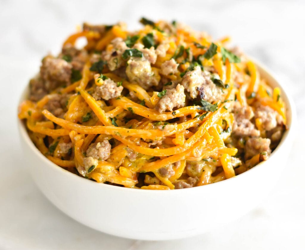 White bowl filled with spiralized butternut squash noodles, creamy parmesan sauce and sausage.