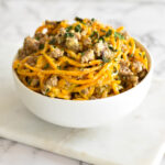 White bowl filled with spiralized butternut squash noodles, creamy parmesan sauce and sausage