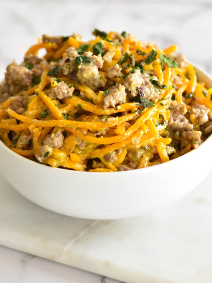 White bowl filled with spiralized butternut squash noodles, creamy parmesan sauce and sausage