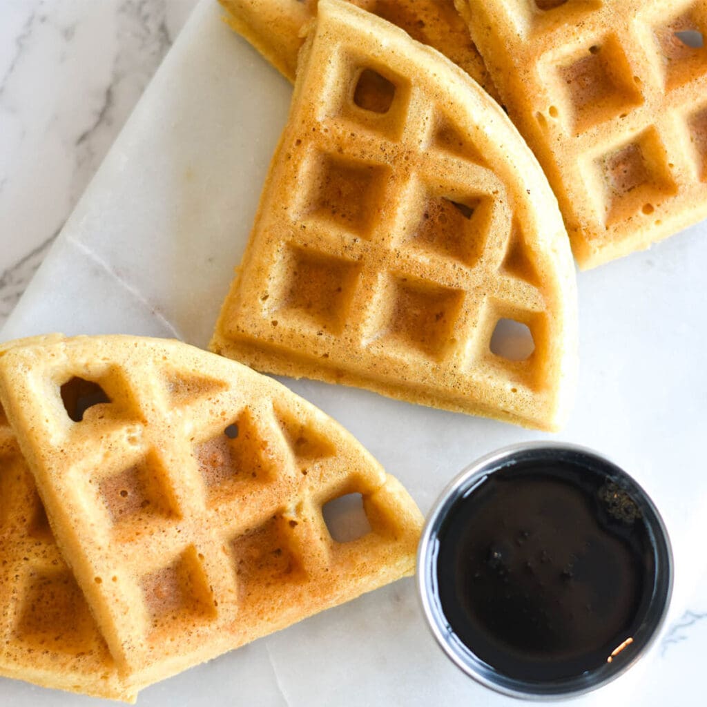 Cut pieces of paleo waffles on cutting board next to syrup for dipping.