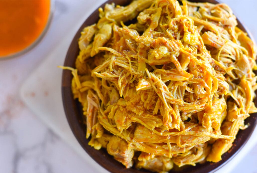 Top down view of shredded chicken with tandoori spices in wooden bowl.