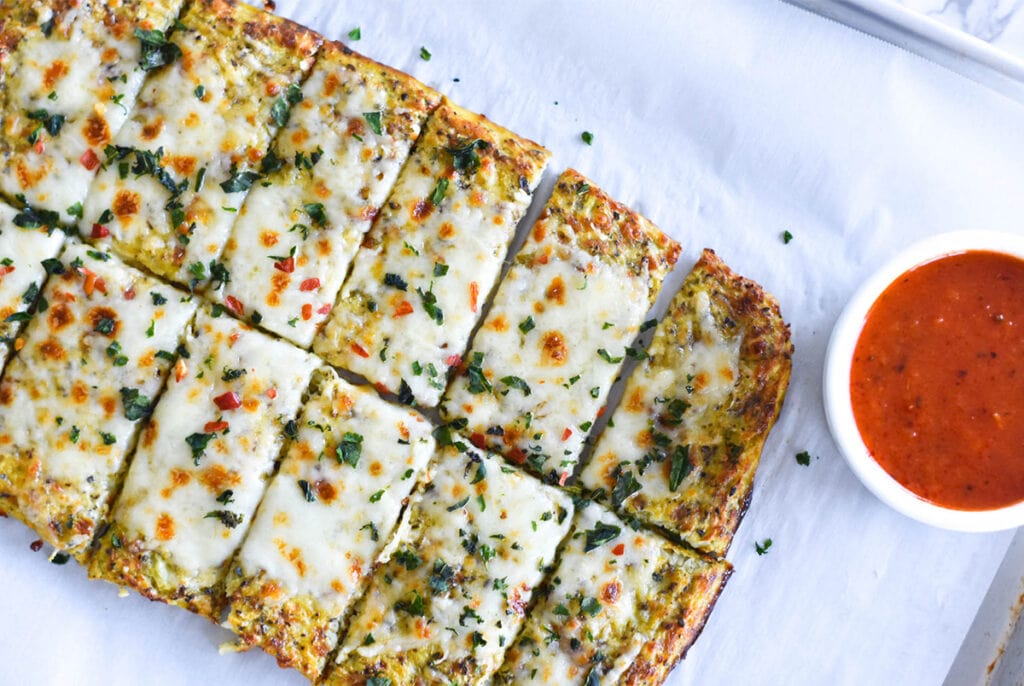 Slices of keto cheesy garlic bread next to some bright red marinara sauce.