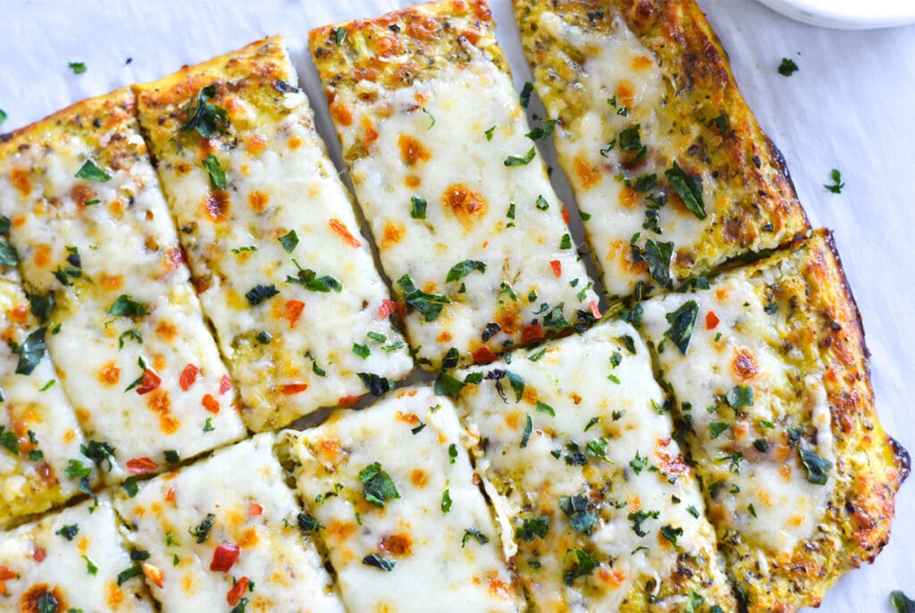 Slices of keto cheesy garlic bread topped with cheese and herbs.