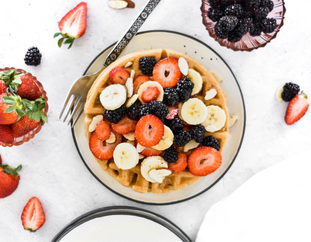 Plate of waffles covered in bananas, blackberries, strawberries and almonds.