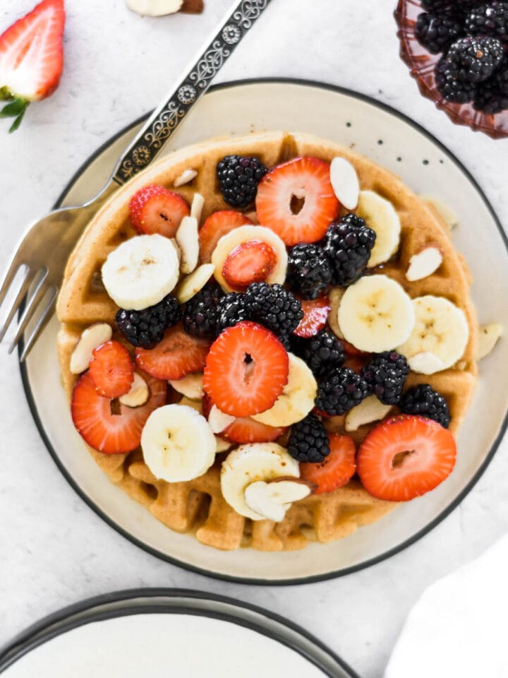 Plate of waffles covered in bananas, blackberries, strawberries and almonds.