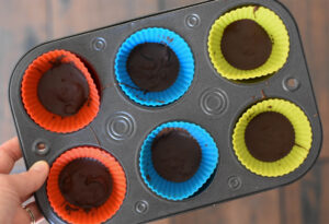 Muffin tin lined with silicone muffin liners filled with a layer of chocolate.