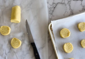 Rolled dough being cut into round slices to make cookies.