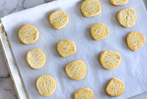 DBaking sheet lined with parchment paper with round buttery shortbread cookies.