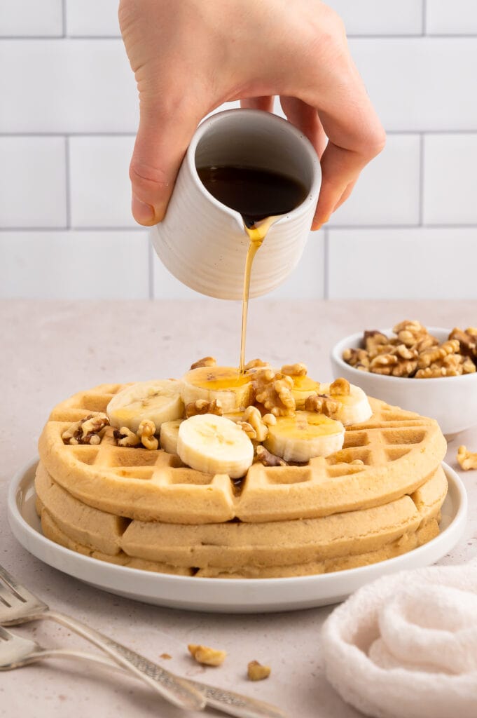 Syrup being poured on crispy paleo waffles with bananas and walnuts.