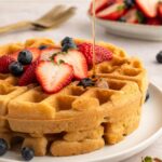 Syrup drizzling over paleo waffles with strawberries and blueberries.