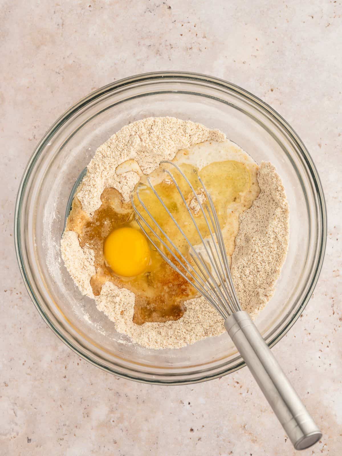Wet ingredients for paleo waffles added to dry ingredients in a mixing bowl with a whisk.