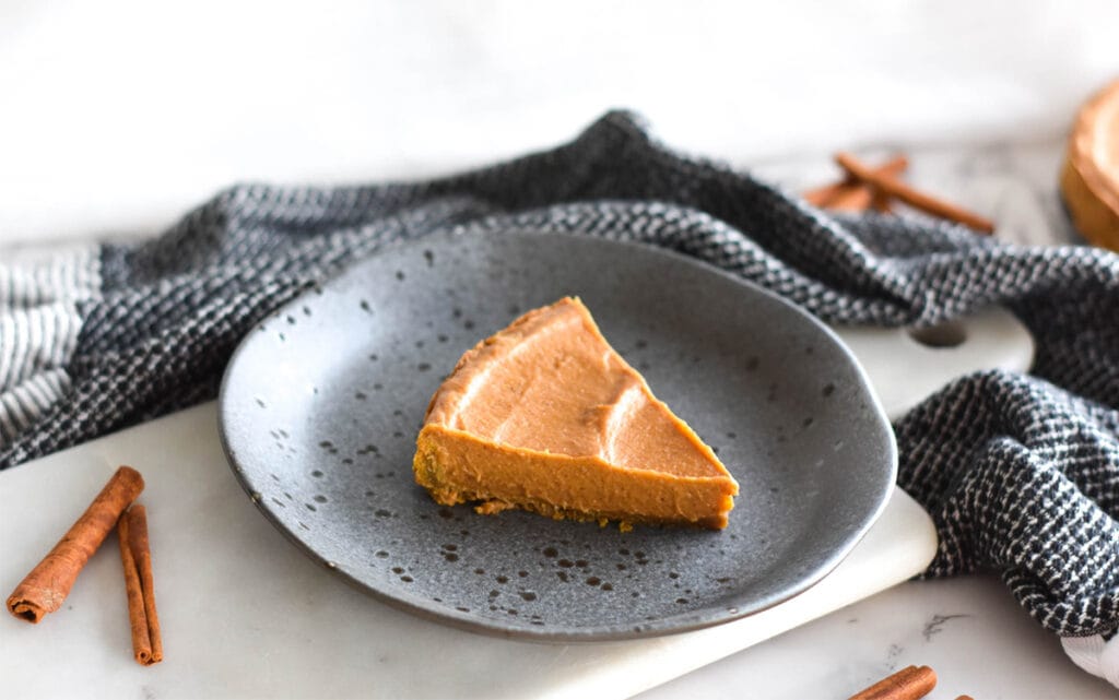 Slice of Paleo AIP pumpkin pie on a stoneware plate next to cinnamon sticks.