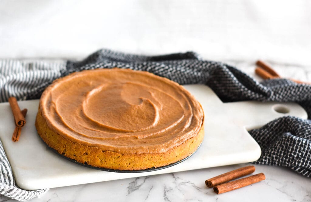 Whole pumpkin pie on cutting board next to cinnamon sticks.