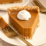 Slice of AIP Pumpkin Pie with coconut whipped cream and a bite on the fork.